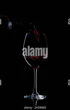 Rotwein wird zu Glas mit langem Stiel in dunklen gegossen Stockfoto