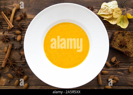 Lecker Kürbis creme Suppe, gemischt mit Gewürzen und Zwiebeln. Ansicht von oben. Herbstliche Stimmung, gelbe Blätter und Karottenkuchen. Braun rustikal Hintergrund. Stockfoto
