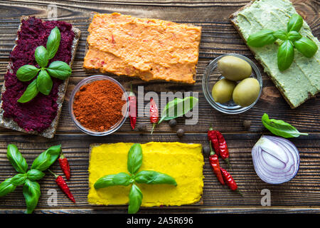 Sortiment von Bruschetta mit Humus auf braunen Tisch. Avocado Geschmack, Curry Geschmack und Frische süße Paprika mit Basilikumblätter, grüne große Oliven und Zwiebel. Stockfoto