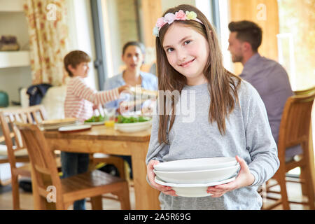 Mädchen hilft mit der Hausarbeit und trägt Gerichte zum Mittag- Stockfoto