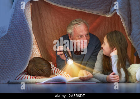 Opa liest Enkelkinder Geschichte unter eine Decke wie ein Zelt zu Hause Stockfoto