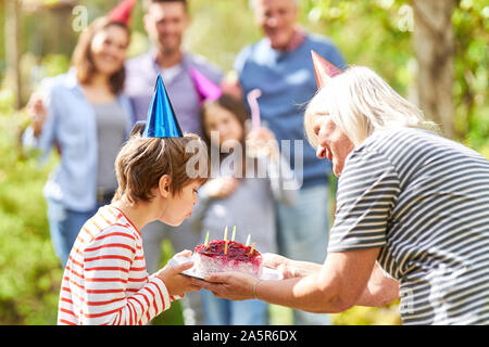 Geburtstag Kind bläst die Kerzen auf der Geburtstagstorte auf Feier im Garten Stockfoto