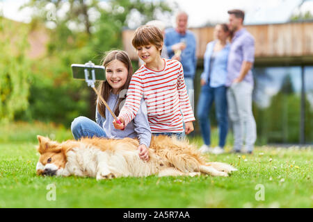 Geschwister Kinder nehmen eine Selfie mit Hund mit der selfie Stick Im Garten Stockfoto