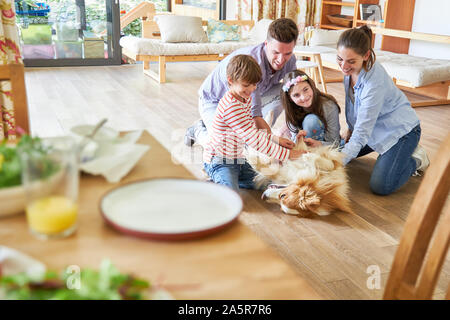 Glückliche Familie und zwei Kinder spielen mit dem Hund im Wohnzimmer Stockfoto