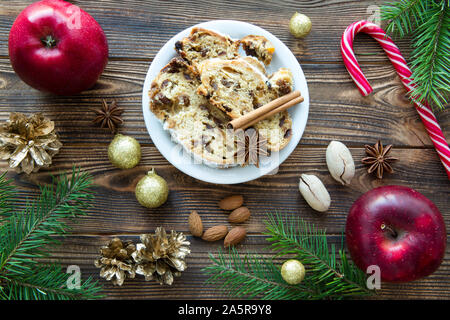 Traditionelle Weihnachten Stollen. Deutsche festliches Dessert auf braune Holztisch Hintergrund. Rote Äpfel, Pecan und Mandeln. Stockfoto