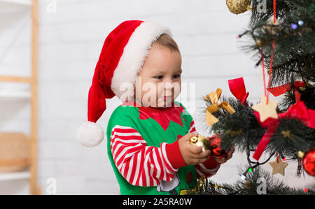 Neugierig Baby in elf Kostüm an Weihnachten Dekorationen suchen Stockfoto