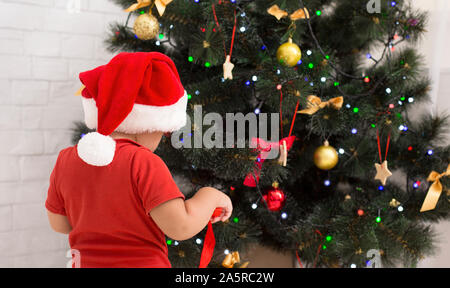 Baby in Santa het Vorbereitung für Urlaub, dekorieren Xmas Tree zu Hause Stockfoto