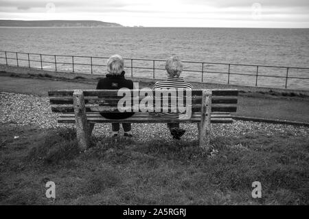 Zwei Damen sitzen auf einer Bank mit Blick auf das Meer. Stockfoto