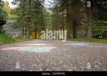 Hellendorf, Deutschland. 17 Okt, 2019. Auf der Asphaltstraße der Ferienanlage am Buschbach in Hellendorf in der Nähe von pirna in Sachsen eine Sonne, eine Wolke mit Regen und Regenbogen sind auf der Straße mit Kreide gemalt. In der Mitte des Waldes gibt es mehrere Hütten. In diese können wie zu DDR-Zeiten Urlaub gemacht werden. Credit: Daniel Schäfer/dpa-Zentralbild/ZB/dpa/Alamy leben Nachrichten Stockfoto