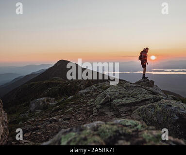 Ein männlicher Wanderer steht auf dem Gipfel eines Berges bei Sonnenuntergang, Maine. Stockfoto