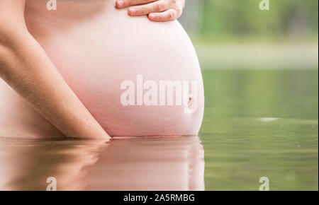 Nahaufnahme von jungen schwangeren Frau mit ihrem Bauch Baden in einem See outdoor. Gesunde natürliche Lebensweise während der Schwangerschaft Konzept Stockfoto