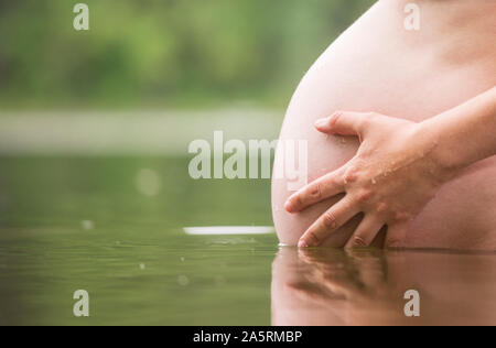 Nahaufnahme von jungen schwangeren Frau mit ihrem Bauch Baden in einem See outdoor. Gesunde natürliche Lebensweise während der Schwangerschaft Konzept Stockfoto