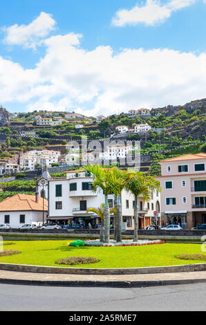 Ribeira Brava, Madeira, Portugal - Sep 9, 2019: Stadtzentrum auf einer vertikalen Bild mit Palmen. Gebäude auf dem Hügel im Hintergrund. Grüne Bäume und Bananenplantagen zwischen den Häusern. Stockfoto