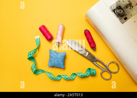 Blick von oben auf die Nähmaschine mit Zubehör zum Nähen, Schere und ein Maßband auf gelbem Hintergrund mit Platz für Text Stockfoto