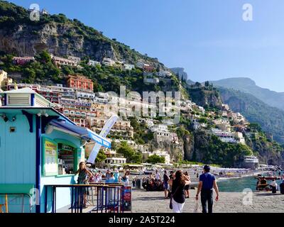 Frau, die vor dem Getränkekiosks und der alternativen Bar steht, während andere sich am Strand der Amalfiküste in der Bergstadt Positano, Italien, entspannen. Stockfoto