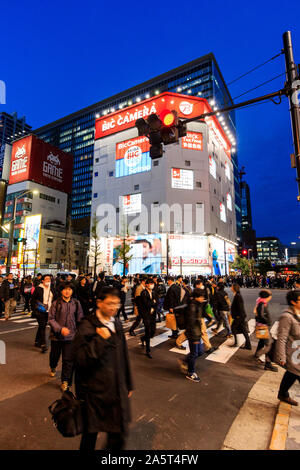 Tokio, Akihabara, der Haupteinkaufsstraße, Chuo-dori. Menschen überqueren die Straße am Zebrastreifen. Bic Camera Gebäude im Hintergrund. Nacht, blaue Stunde. Stockfoto