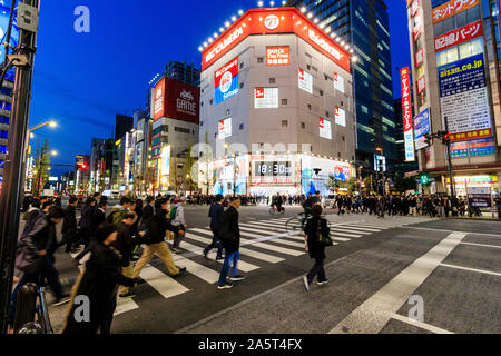 Tokio, Akihabara, der Haupteinkaufsstraße, Chuo-dori. Menschen überqueren die Straße am Zebrastreifen. Bic Camera Gebäude im Hintergrund. Nacht, blaue Stunde. Stockfoto