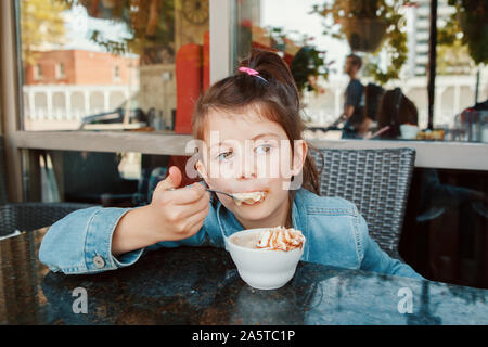 Lustige kaukasischen Vorschule Mädchen essen süßes Dessert mit Löffel im Cafe. Kind Spaß im Restaurant Terrasse Essen trinken. Gerne verbindlich Stockfoto