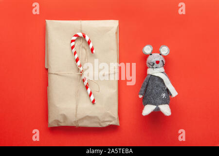 Grau Spielzeug Ratte, das Symbol des 2020 von den chinesischen Kalender und Weihnachten Geschenk verpackt in Handwerk Papier, mit Zuckerrohr candy auf rotem Hintergrund eingerichtet. Minimal Style Stockfoto