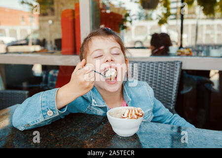 Lustige kaukasischen Vorschule Mädchen essen süßes Dessert mit Löffel im Cafe. Kind Spaß im Restaurant Terrasse Essen trinken. Gerne verbindlich Stockfoto