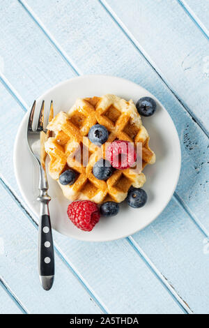 Waffeln mit Heidelbeeren und Himbeeren auf die Platte an der blauen Tabelle. Ansicht von oben. Stockfoto