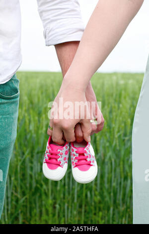 Eine Frau und ein Mann die Schuhe halten Baby. Eine Frau und einen Mann halten die Schuhe der Kinder auf der Wiese im Freien. Ein Baby erwartet konzeptionelle Bild. Stockfoto