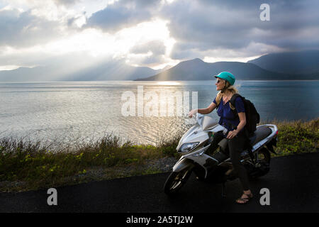 Eine Frau sitzt auf einem Motorrad mit wunderschönen Ozean Szene im Hintergrund. Stockfoto
