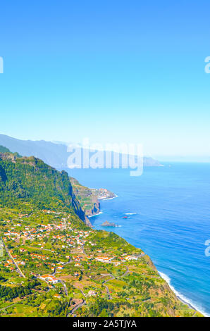 Erstaunlich Nordküste der portugiesischen Insel Madeira. Sao Jorge Village inmitten grüner Hügel und tropischer Wald umgeben, Felsen durch den Atlantischen Ozean. Blick vom Aussichtspunkt auf dem Gipfel des Hügels. Stockfoto