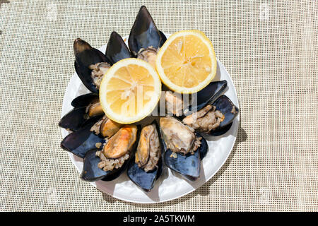 Blick von oben auf einen Teller Gefüllte Miesmuscheln durch zwei Hälften eines saftig gelbe Zitrone an einem sonnigen Tag begleitet. Stockfoto