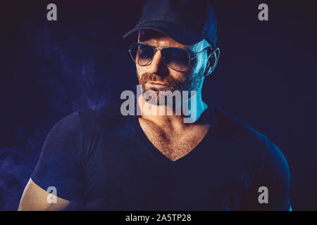 Portrait von brutalen bärtigen Mann in sunglassesand Baseball Cap an dunklen Photo Studio. Stockfoto