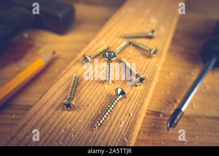 Schrauben, Schraubendreher, Hammer und einen Bleistift auf einen hölzernen Tisch. Konzept Werkzeuge und Reparaturarbeiten. Stockfoto