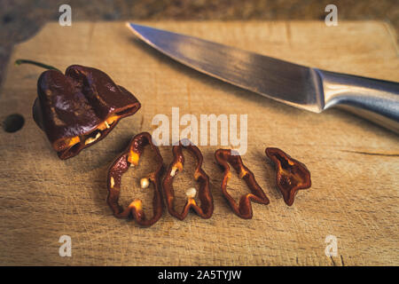 Schokolade Habanero Pfeffer (Capsicum chinense) Schichten auf einem Holz Schneidebrett und Chrom Messer. Gesunde und wirklich hot chili peppers. Stockfoto