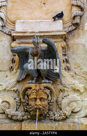 Schwarze Taube sitzend auf öffentlichen Trinkbrunnen, mit Skulpturen von Adler und männliche Gesicht dekoriert Stockfoto