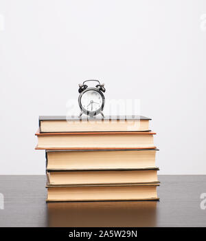 Stapel von Büchern und einem schwarzen Wecker auf dem Tisch, weißer Hintergrund, Kopie Raum Stockfoto