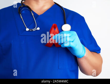 Arzt in der blauen Uniform und sterile Latex Handschuhe hält ein Red Ribbon - ein Symbol für den Kampf gegen die Krankheit AIDS und Vaskulitis Stockfoto