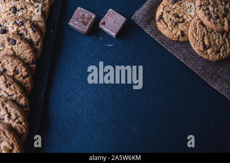 Traditionelle Chocolate Chip Cookies und Stücke von Kakao auf einer Schiefertafel Tabelle. Ansicht von oben Kochkurs Plakat Hintergrund - Layout mit freiem Text spa Stockfoto