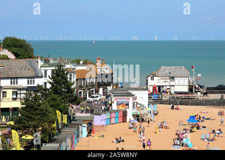 Die Menschen genießen den Strand in Broadstairs und seine Strandpromenade Annehmlichkeiten. Sieben Meilen heraus sind die 100 Turbinen der Thanet Windpark in Betrieb genommen im Jahr 2010 Stockfoto