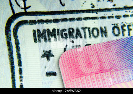 UK BRP Stufe 2 Visa Card auf Einreisestempel im Pass, wo nur Buchstaben "EINWANDERUNG AUS' von Phrase der "Immigration Officer' sichtbar. Stockfoto