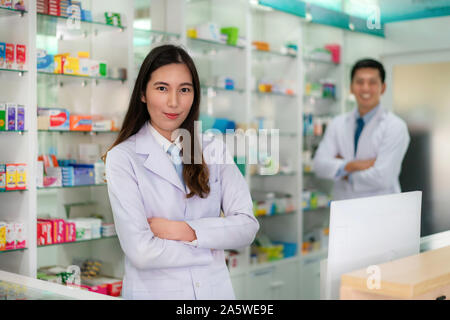 Zwei Asiatische junge Frau und Mann Apotheker mit einem reizenden Lächeln stand mit verschränkten Armen in der Apotheke und Drogerie. Medizin, Pharmazie, er Stockfoto