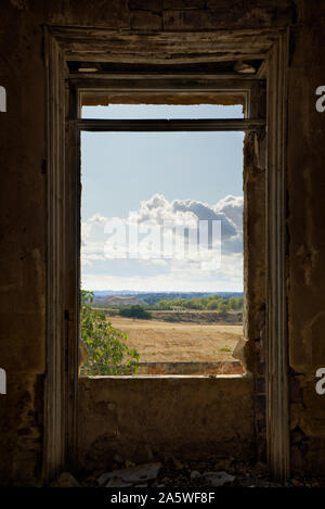 Blick auf eine Wiese und bewölkter Himmel über einem maroden Fenster Stockfoto