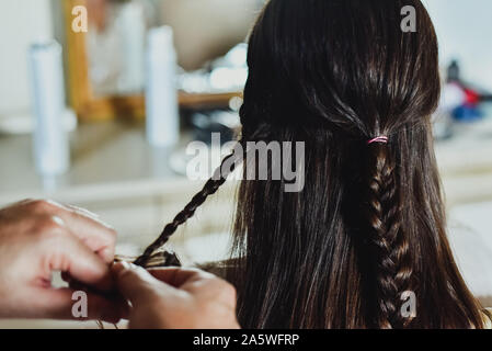 Ein Friseur macht Zöpfe in die Haare der Eine brünette Frau. Stockfoto