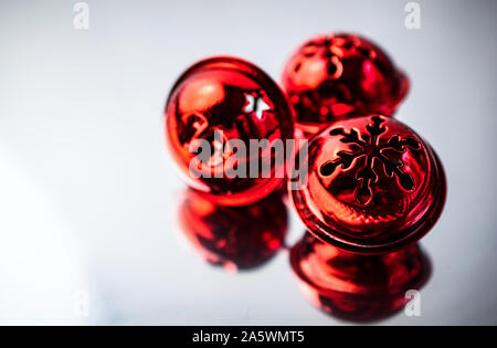 Nahaufnahme von drei Red Christmas Jingle Bells isoliert auf Silber reflektierende Oberfläche Stockfoto