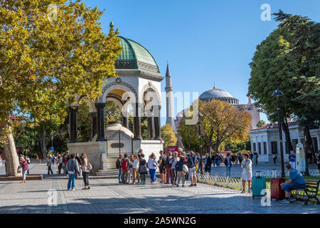 Touristen Pass von der Deutschen Brunnen, ein Pavillon gestaltete Brunnen in Sultanahmet Square mit der Hagia Sophia in der Ferne Stockfoto