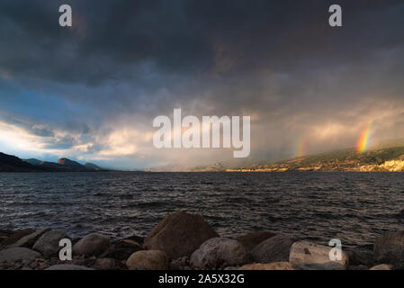 Blick auf dramatische Gewitterwolken und doppelten Regenbogen über den Okanagan Lake, BC, Kanada Stockfoto