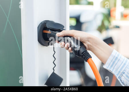 Junge erwachsene Frau mit Power Kabel zum Aufladen von Elektroautos Stockfoto