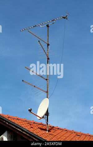 Fünf TV-Antennen neben einer Satellitenschüssel auf einzelne metallmast montiert auf der neuen Familie Haus Dach auf klaren, blauen Himmel Hintergrund Stockfoto