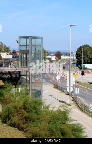 Aufzug aus Glas an der Seite der Bahnhof mit dichter Vegetation und Straße unter Rekonstruktion mit mehreren Warnung Verkehrszeichen umgeben Stockfoto