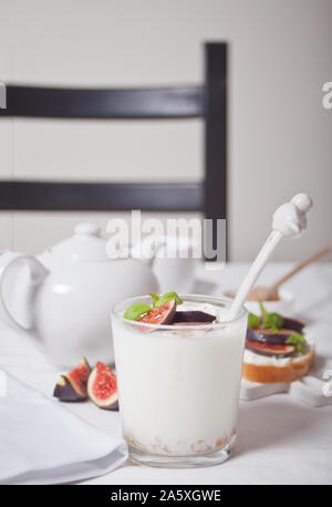 Joghurt mit Müsli und Obst, Sandwich mit Frischkäse, Feigen und Honig auf den weißen Hintergrund. Gesunde Ernährung Konzept. Stockfoto