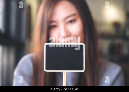 Eine schöne asiatische Frau mit ein leeres Quadrat Tafel mit unscharfen Hintergrund Stockfoto