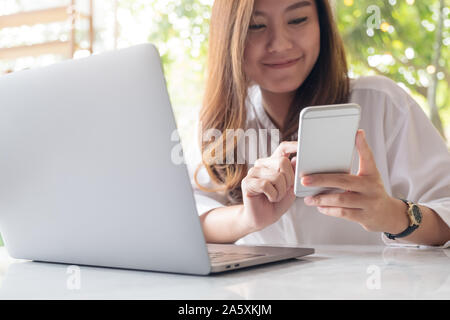 Closeup Bild eines schönen asiatischen woman holding und Smart Phone, während mit Laptop im Cafe Stockfoto